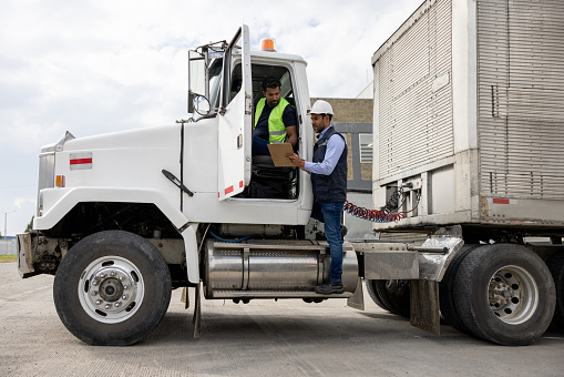 Foreperson supervising the transportation of merchandise at a distribution warehouse and talking to a truck driver