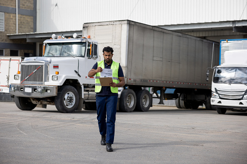 Latin American foreperson working at a distribution warehouse supervising the shipping of merchandise in trucks - freight transportation concepts