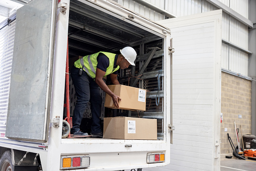 African American man working at a distribution warehouse loading boxes on a truck - freight transportation concepts