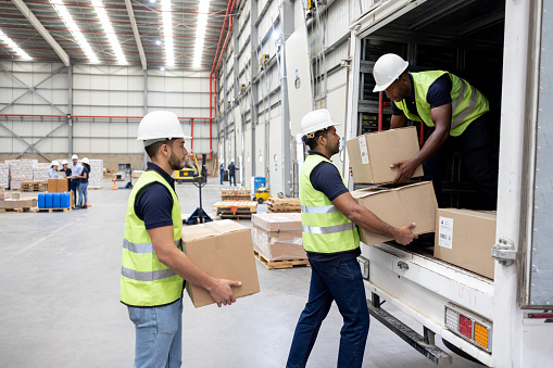 Group of workers working at a distribution warehouse loading boxes on a truck - freight transportation concepts