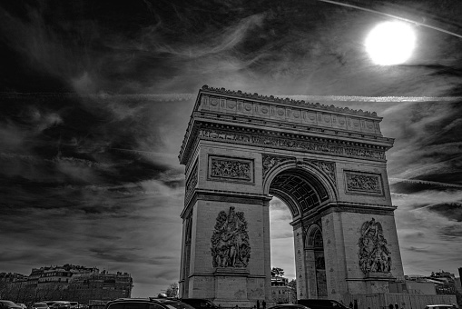 Arc de Triomphe and dramatic cloudscape with the bright sun in Paris, France, monochromatic high contrast black and white photography