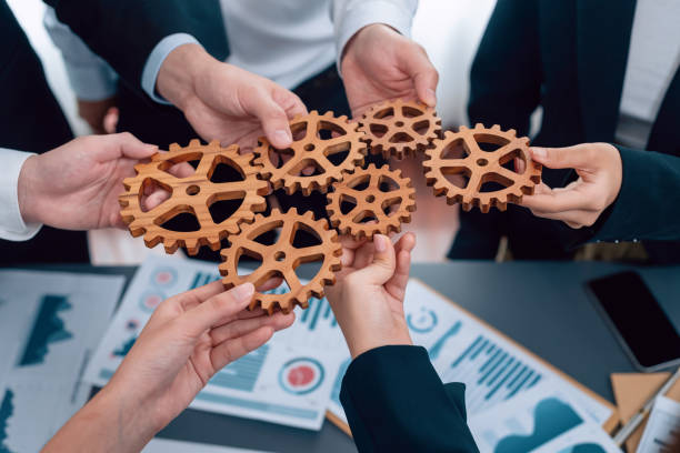istock Closeup top view hands holding gears over table with BI reports for harmony. 1474053561