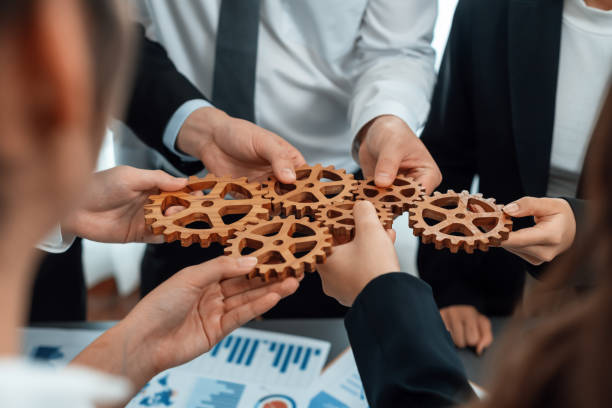 istock Closeup top view hands holding gears over table with BI reports for harmony. 1474053587