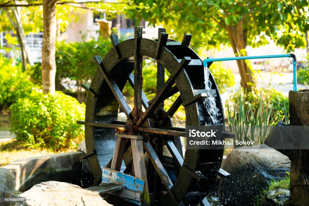 A working watermill wheel with falling water on a background of green trees on a clear sunny day A working watermill wheel with falling water on a background of green trees on a clear sunny day. Mill Stock Photo