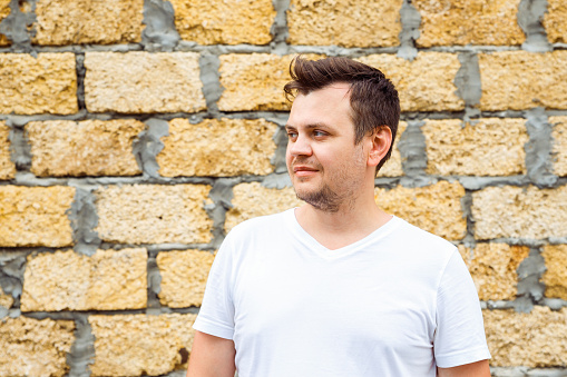 male man in white t-shirt on yellow limestone laid bricks wall background. Lifestyle looking away unshaven profile view young caucasian man portrait, close-up. Entrepreneur, businessman