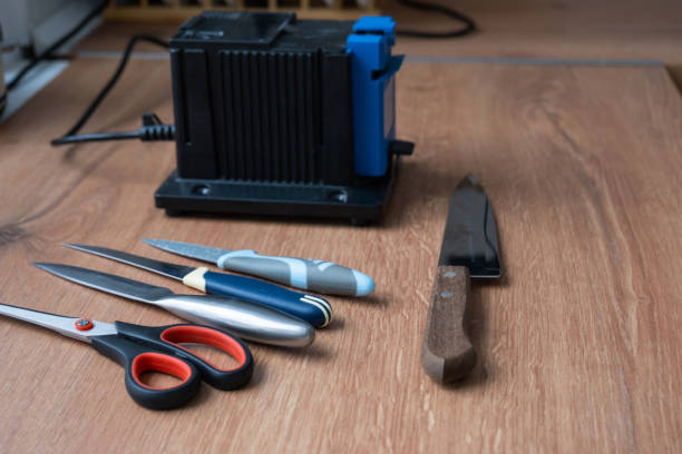 istock Sharpening a knife on an electric sharpener at home. Flatlay knife blade, scissors, sharpeners, dust flies on the machine. 1474069463