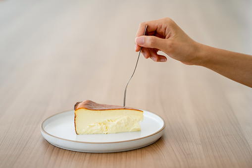 Crop  Asian woman hand holding fork towards a slice of cake