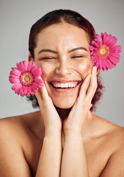 Natural beauty, flowers and face of happy woman with eco friendly makeup, facial product or floral skincare glow. Sustainable cosmetics, spa salon girl and model smile isolated on studio background Natural beauty, flowers and face of happy woman with creative facial design, floral product and healthy skincare glow. Makeup cosmetics, spa salon girl and model smile isolated on studio background makeup product photography stock pictures, royalty-free photos & images