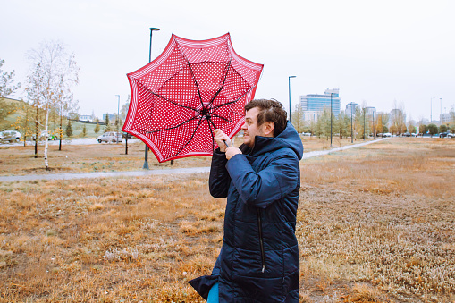 wind, storm, rain, bad weather. shocked european young male man with broken umbrella in autumn park.