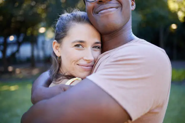 Photo of Interracial relationship hug, park and woman with smile, care and love with black man, reunion and happiness. Multicultural embrace, happy couple and diversity on nature adventure, bonding and spring