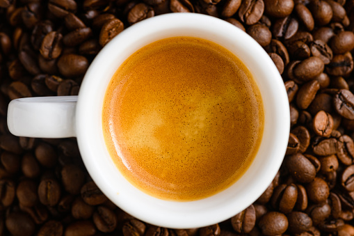 Top view of brewed espresso in a cup at whole roasted coffee beans background