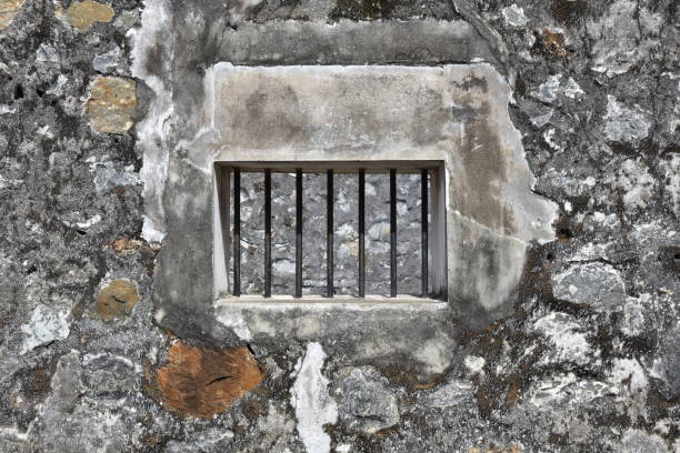 ventana enrejada en piedra y muro de concreto de la prisión - barred windows fotografías e imágenes de stock