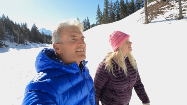 istock Mature couple walk along snowy path in mountain  setting 1474082247