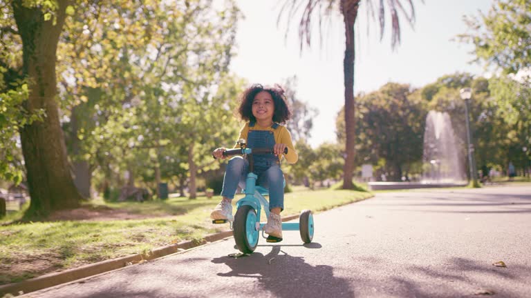 Cycling, park and girl on tricycle in sunshine enjoying freedom, summer holiday and weekend outdoors. Travel, childhood and young African child relax, smile and excited to ride bicycle for wellness