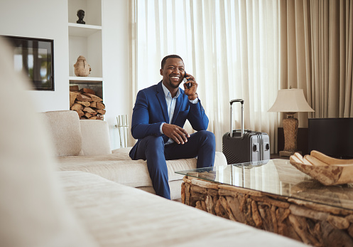 Happy businessman in hotel, on smartphone call and business communication for work in Atlanta. Young black entrepreneur, listening to audio on cellphone and sitting on luxury sofa in living room