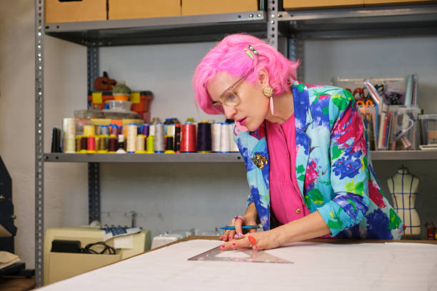 istock Tailor with pink hair and colorfull clothes drawing sewing patterns. 1474089255