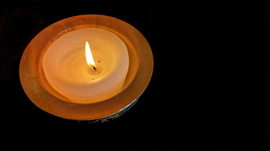 Burning candle on the old brass candlestick over black background