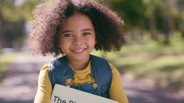 Portrait, book and education with a black girl in the park, looking happy during back to school season. Kids, face and learning with a young child student standing outdoor in a garden in the morning