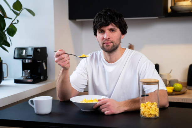 istock Young man eats cornflakes for breakfast at the table in the kitchen at home 1474092241