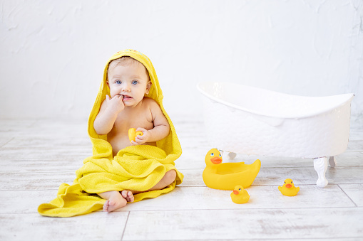 cute little baby girl under a yellow towel in the bathroom after bathing or washing, baby hygiene concept