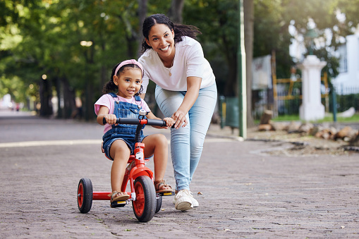 Mother, kid and bicycle teaching with training wheels for learning, practice or safety at the park. Happy mom helping little girl to ride a bike with smile for proud playful moments in the outdoors