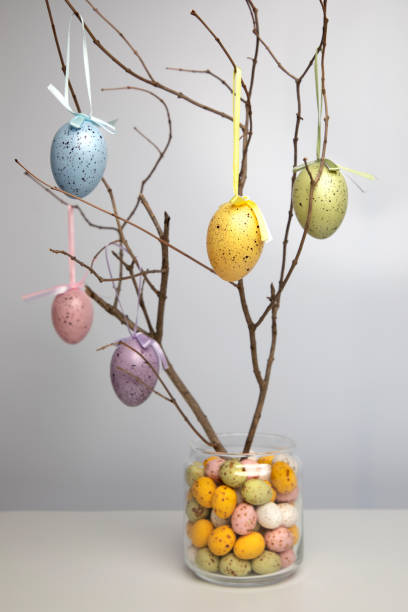 istock Chocolate colorful decorative eggs in a glass jar and wooden branches decorated with eggs on a white background. Happy Easter 1474099698