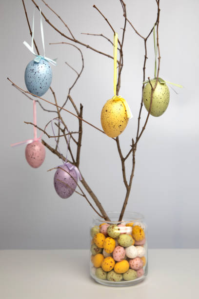 Chocolate colorful decorative eggs in a glass jar and wooden branches decorated with eggs on a white background. Happy Easter stock photo