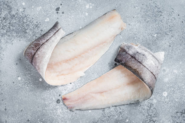 Two raw haddock fish fillets on kitchen table. Gray background. Top view