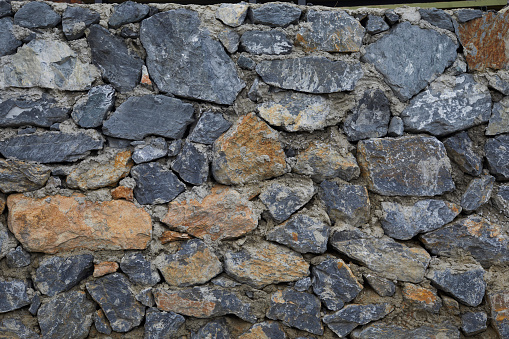 Straight wall background texture. Irregular and random stone pattern. Large rock pattern texture with many hues of grey, yellow, red and blue. Selective focus.