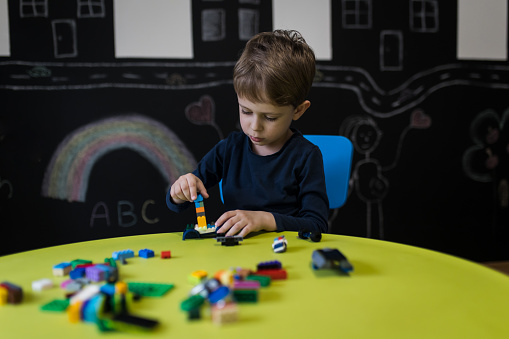 Little boy playing with colourful educational toy blocks on the table. Kid having fun while engaged in creative learning and development