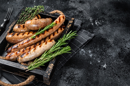 sausages and ingredients for cooking. Grilled sausage with the addition of herbs and and spices, vegetables, rosemary, thyme on the grill plate, Grilling food, bbq, barbecue, on stone table. Top view.