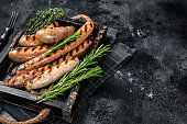 Fried on a grill skillet mix sausages in a wooden tray with herbs. Black background. Top view. Copy space