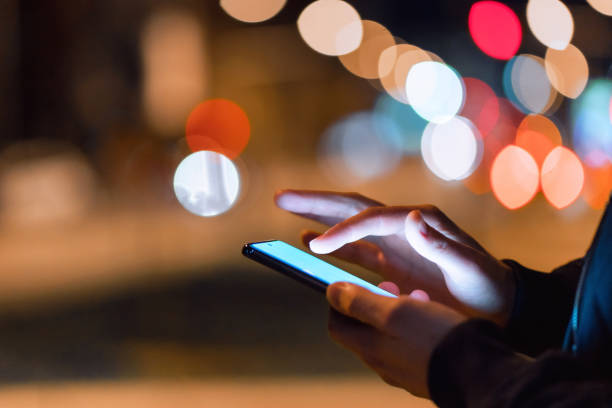 Using a smartphone in the city at night Close-up shot of a man using a phone in the city at night. mobile phone lights up stock pictures, royalty-free photos & images