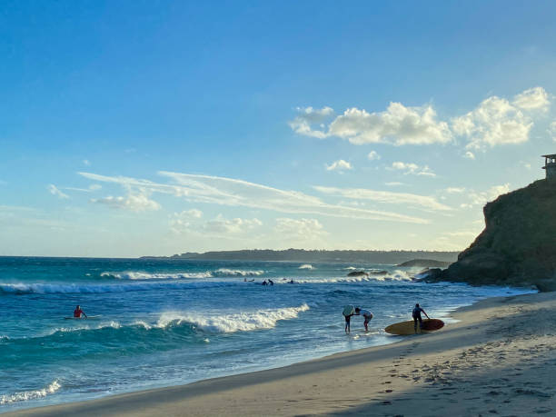 The sky is not yet dark, and there are still blue sky and white clouds. Surfers finish their practice and return to the shore with their surfboards, ready to rest