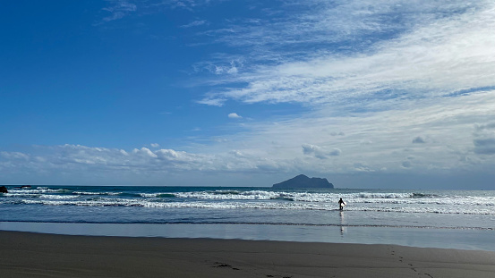 A surfer is walking into the sea with a surfboard to practice with blue sky and white clouds