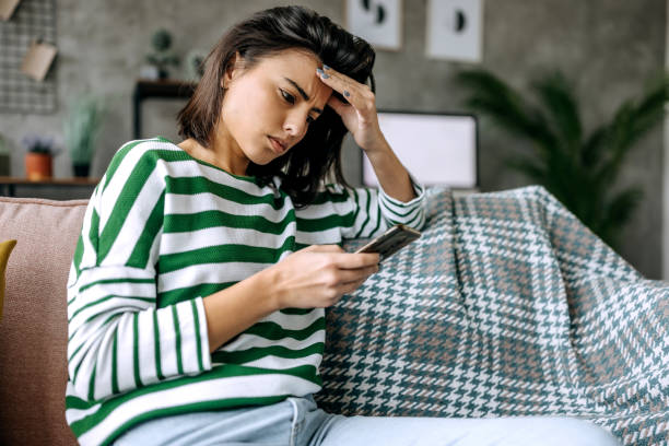 istock Concerned young woman using smart phone in a living room 1474111396