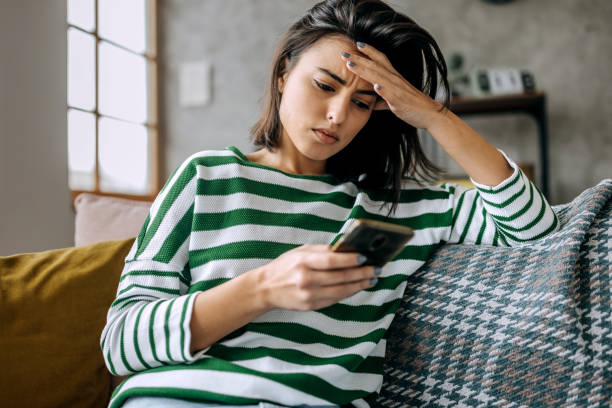istock Concerned young woman using smart phone in a living room 1474111418