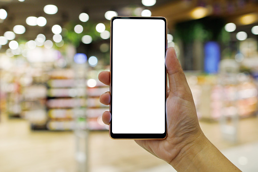 Cropped shot of female hand holding a blank screen phone against a modern shopping mall background