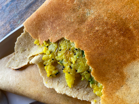 Stock photo of a breakfast meal with an Indian masala dosa, a thin potato pancake that is folded and filled, it is being served on a white plate and has been cut open