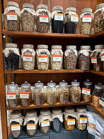 Stock photo showing pantry with an assortment of glass jars full of various dried ingredients, including pasta, beans, seeds, lentils, pulses and spices. These jars are lined up and organised neatly on shelves for ease of access, with labels on them.