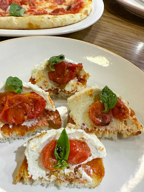 image rapprochée de la table du restaurant, entrée bruschetta sur assiette blanche, tranches de pain baguette, fromage mozzarella, tomates cerises hachées à l’ail et sauce pesto de base, arrosée de vinaigre balsamique, garniture de feuilles de basil - baguette vinegar balsamic vinegar glazed photos et images de collection