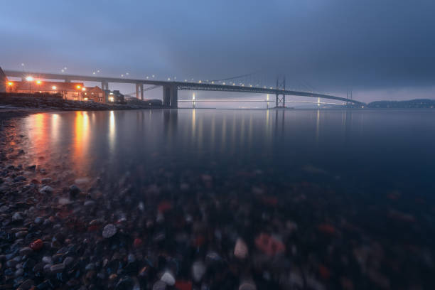 Two bridges covered in thick fog at sunset in winter, and colourful stones in the foreground stock photo