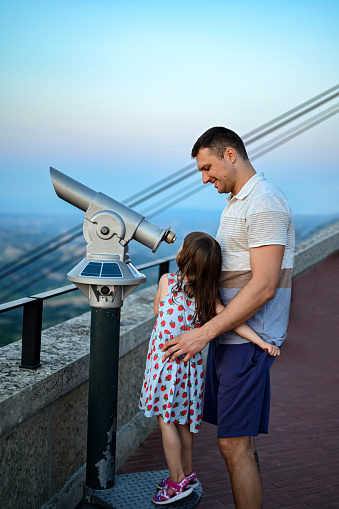 Father and daughter looking through the telescope from the top of mountain during travelling