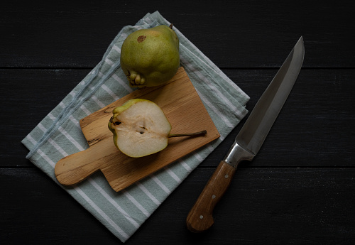 Pears and half of pear on a cutting board on wooden planks with textile napkin