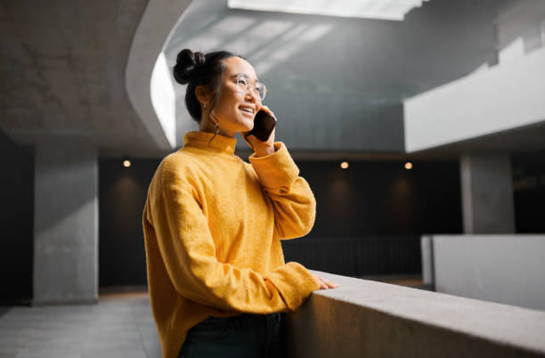 istock Phone call, networking and mockup with an asian woman talking while standing in a hallway. Mobile, communication and conversation with an attractive young female speaking on her smartphone indoor 1474125568