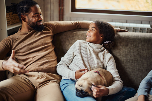 Happy African American daughter communicating with her single father in the living room.