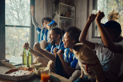 Cheerful African American family celebrating success of their sports team while watching a game on TV at home.