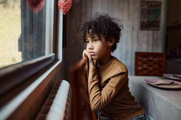 Sad black boy looking through window from home.