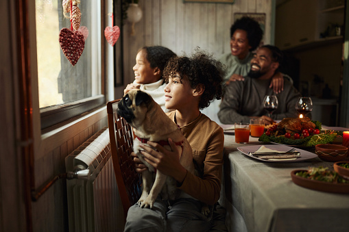 Happy African American family enjoying while looking through window during lunch at dining room. Focus is on boy.