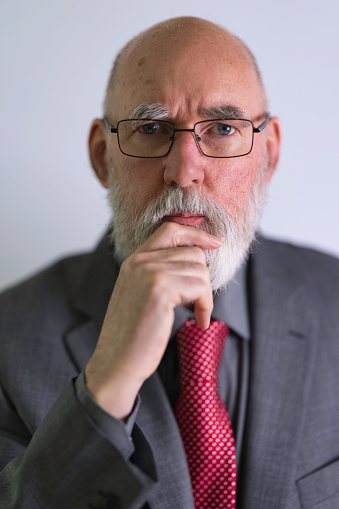 Bald Caucasian man in his 70s with a beard, wearing a formal suit, shirt and tie.